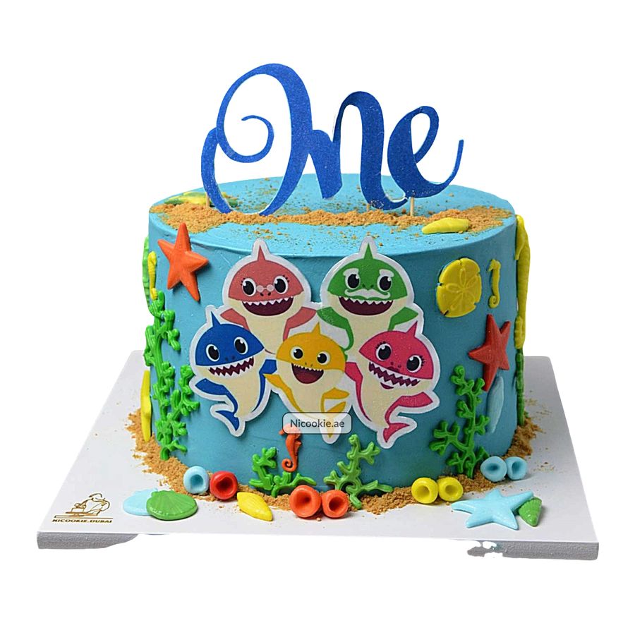 A blue Baby Shark themed cake with the word "One" on top.