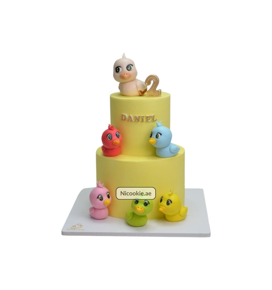 A two-tiered yellow cake decorated with fondant ducklings and the name Daniel.