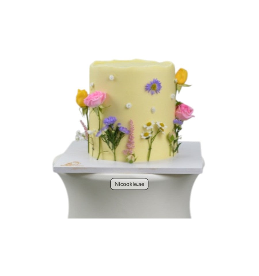 A yellow cake decorated with fresh flowers and small white dots.