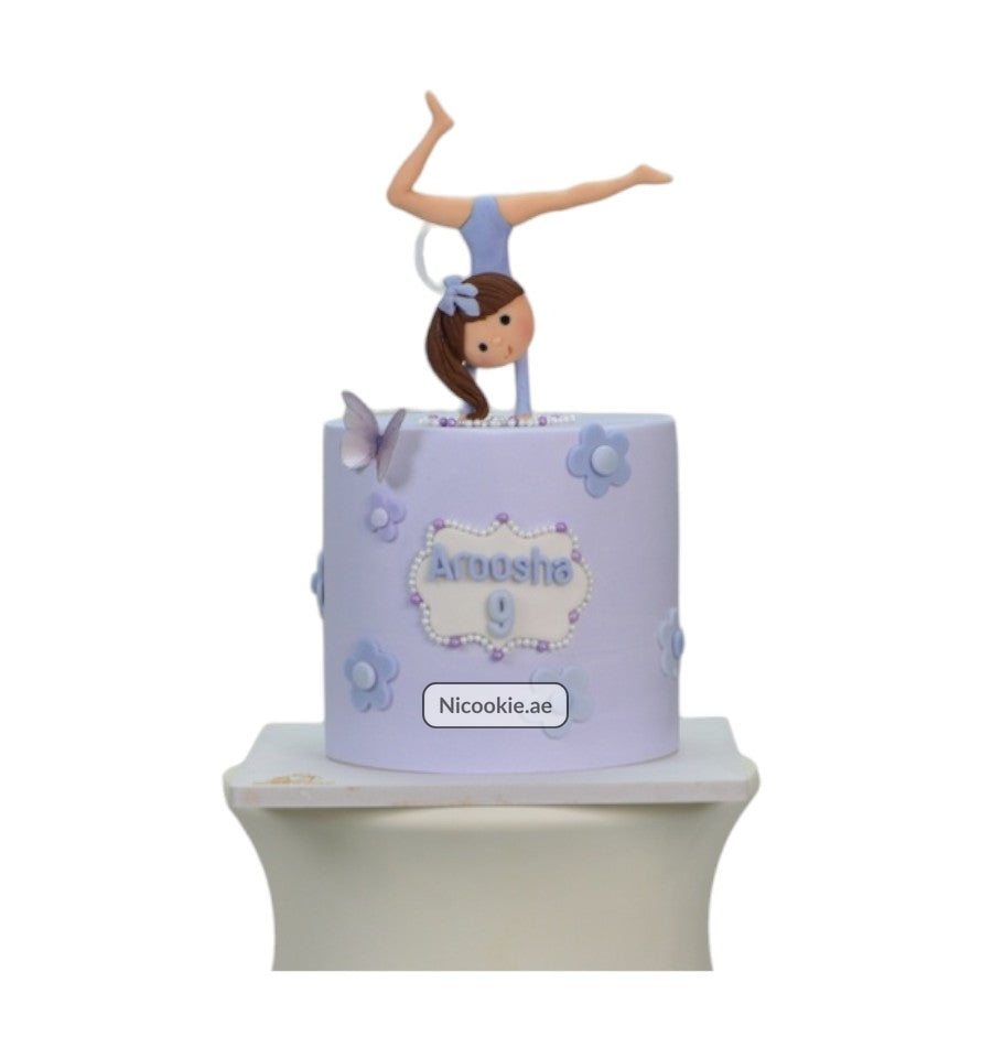 Lilac cake with a gymnast topper, floral decorations, and the name Aroosha.