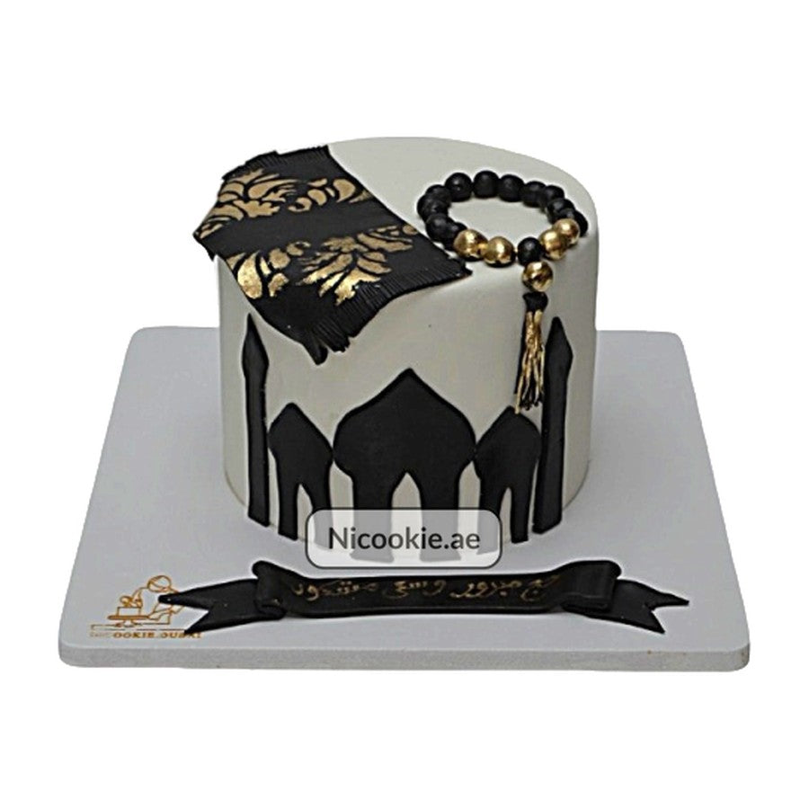 A white cake decorated with a mosque silhouette, prayer mat, and prayer beads.