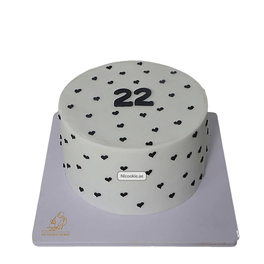 Round white cake with black hearts and the number 22.