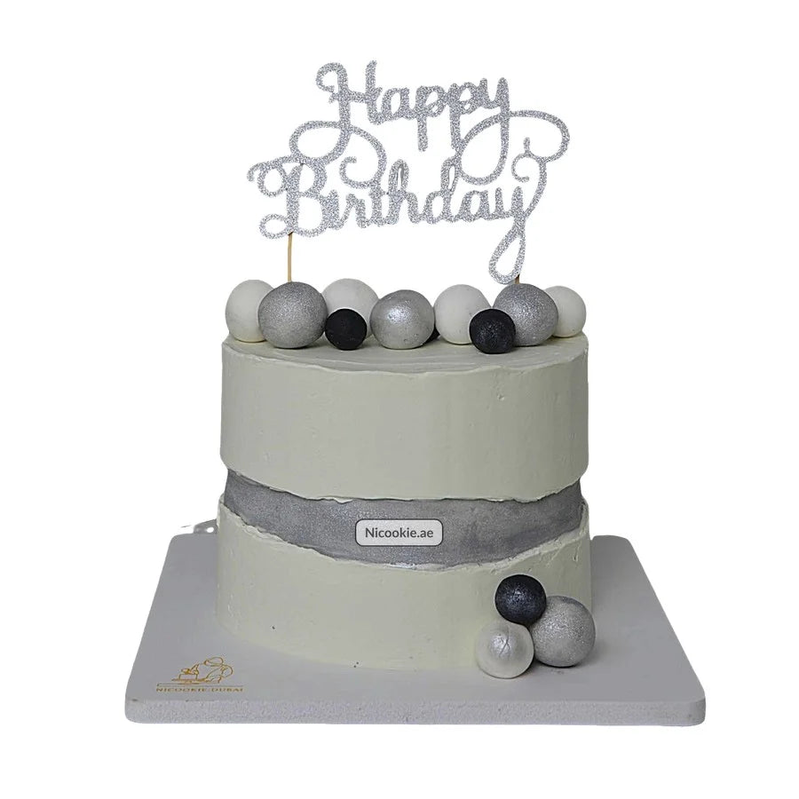 A modern white birthday cake with a silver band and spherical decorations.
