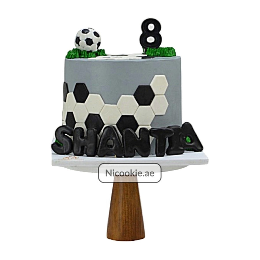 A soccer-themed cake with a football design, soccer ball topper, and the name "SHANTIA".