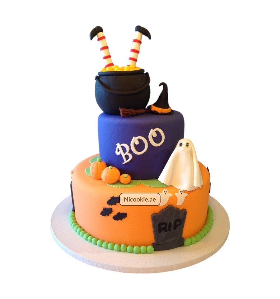A two-tiered Halloween cake with a witch's cauldron, ghost, and pumpkins.
