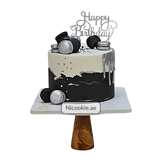 Black and silver birthday cake with macarons and a "Happy Birthday" topper.