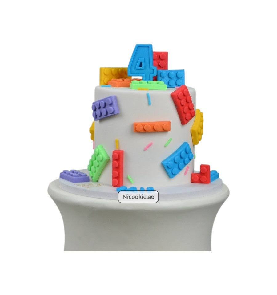 A white cake decorated with colorful building blocks and a blue number 4.