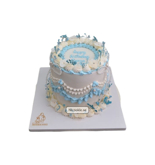 A blue and white cake decorated with pearls and floral accents.