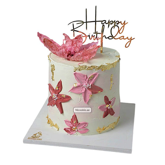A blush pink floral cake with gold accents and a "Happy Birthday" topper.