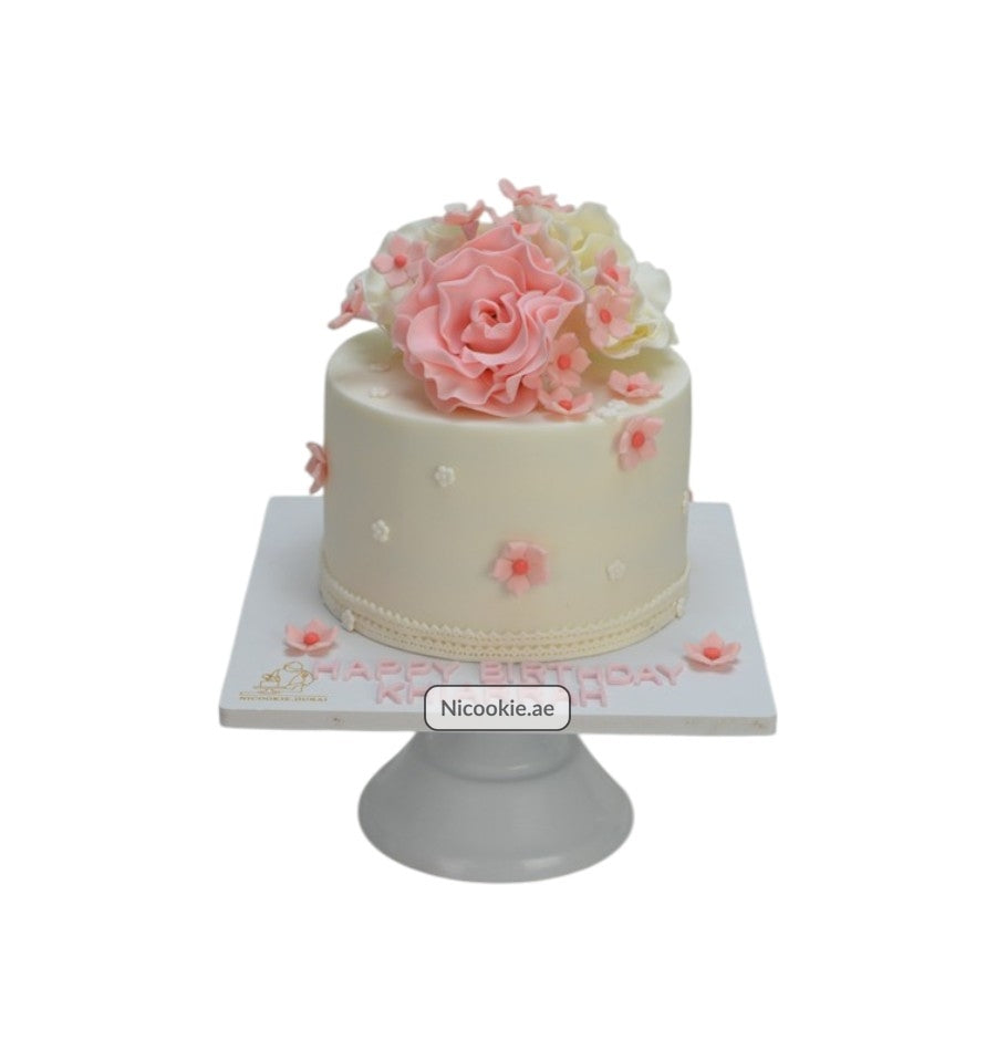 White cake with pink and white sugar flowers and "Happy Birthday" text.