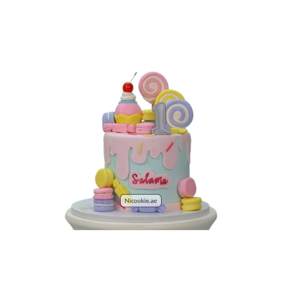 A Candyland themed cake with colorful candies, macarons, and a cherry topper.