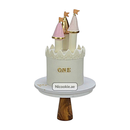 Castle-themed first birthday cake with fondant towers and gold "ONE" lettering.