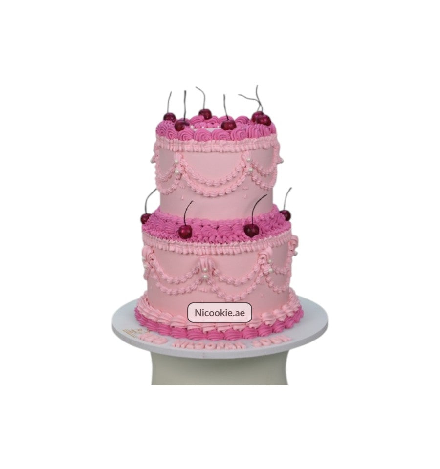 A two-tiered pink cake decorated with cherries and intricate frosting details.