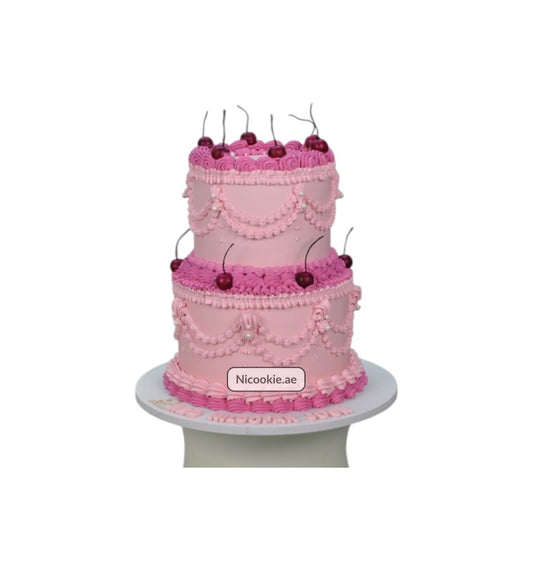 A two-tiered pink cake decorated with cherries and intricate frosting details.