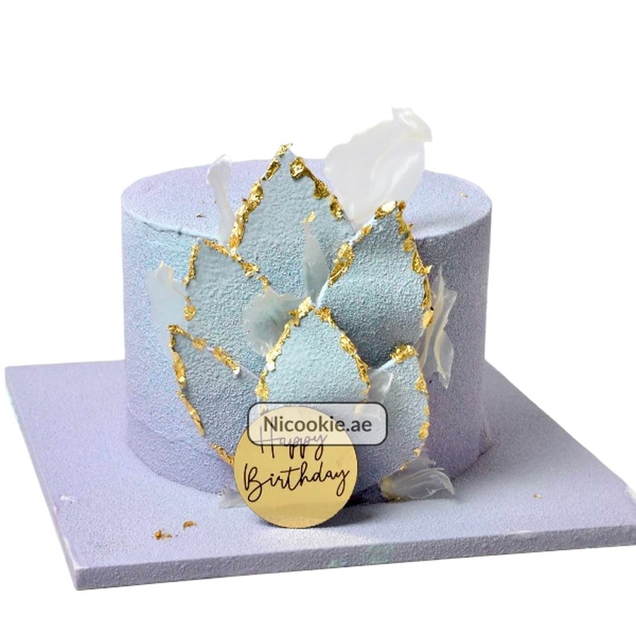 Lavender cake with blue petals and gold accents, topped with a "Happy Birthday" topper.