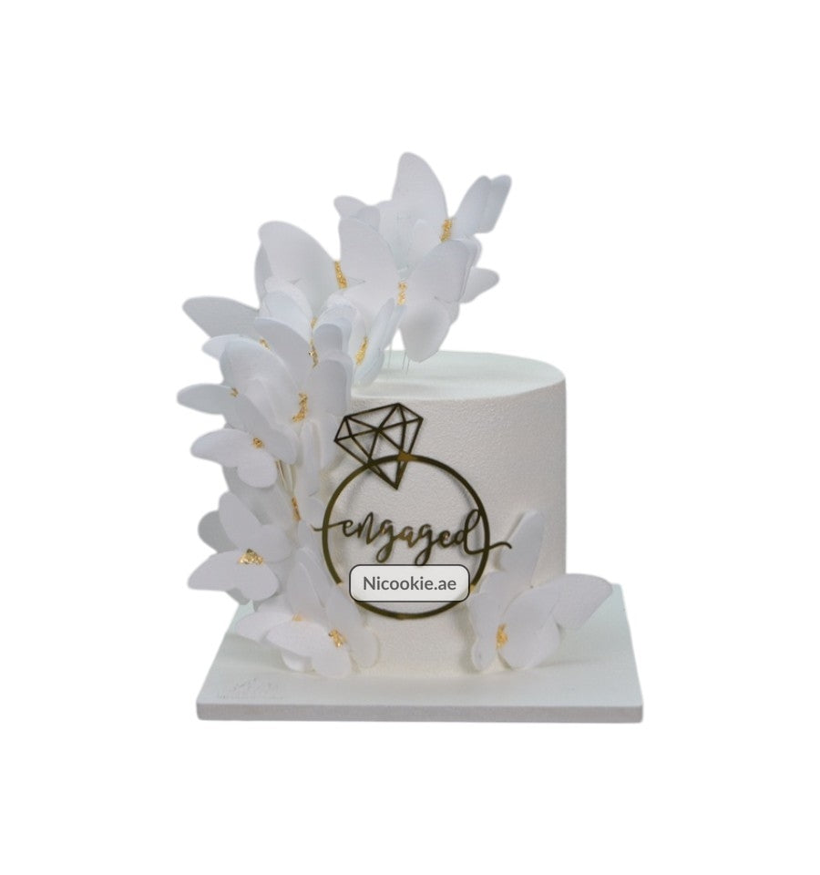 White engagement cake with butterflies and a diamond ring topper.