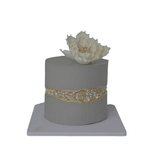 A gray fault line cake with gold and pearl beads and a white flower.