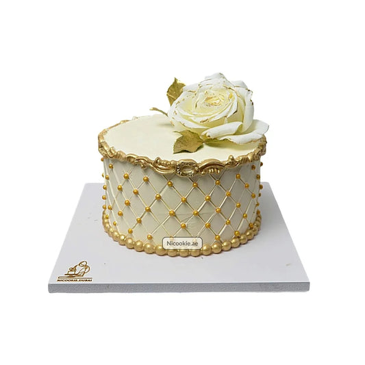 A white cake with a quilted pattern, gold pearls, and a white rose.
