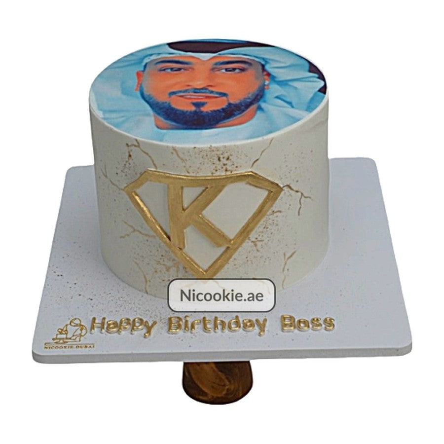 A round cake with a portrait on top and a gold monogram on the side.