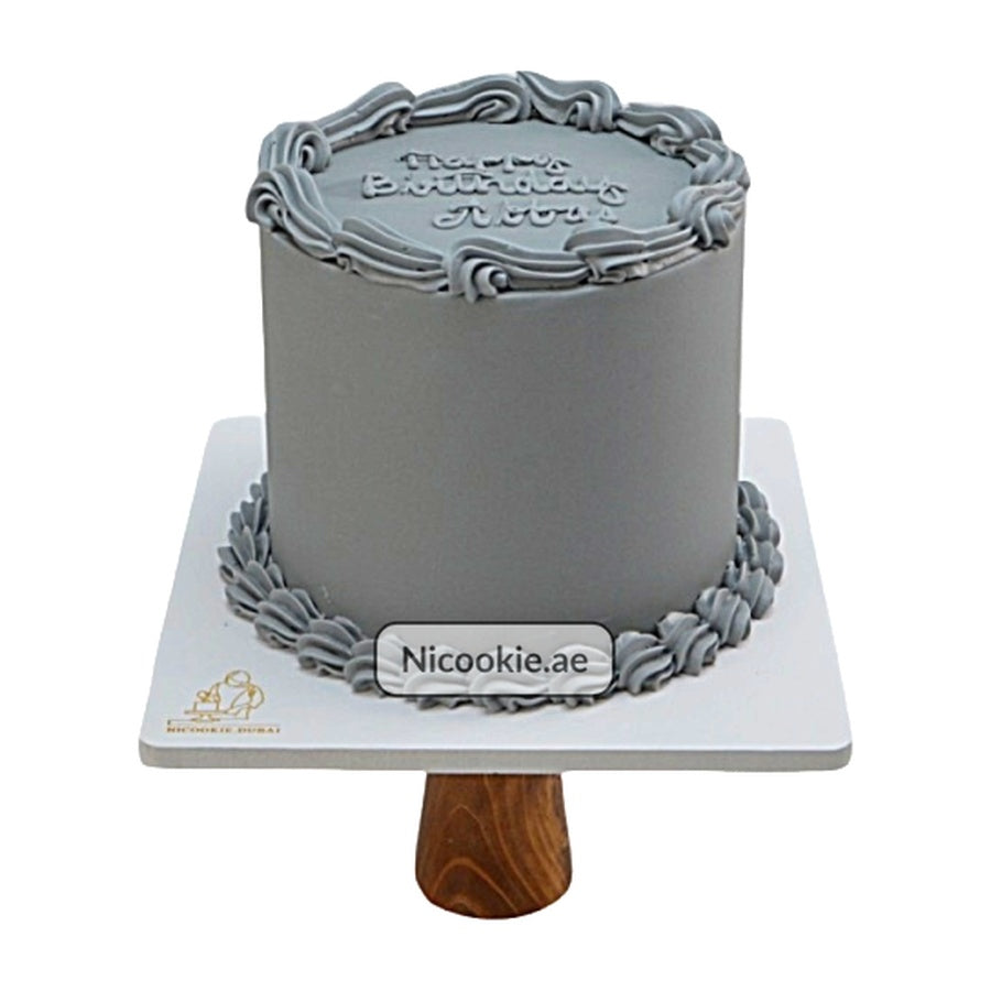 A grey birthday cake with piped frosting and a message on top.