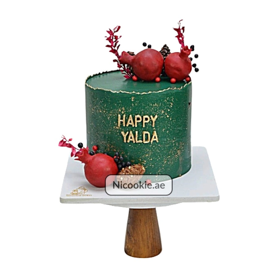 A green Yalda cake with pomegranates and gold lettering.
