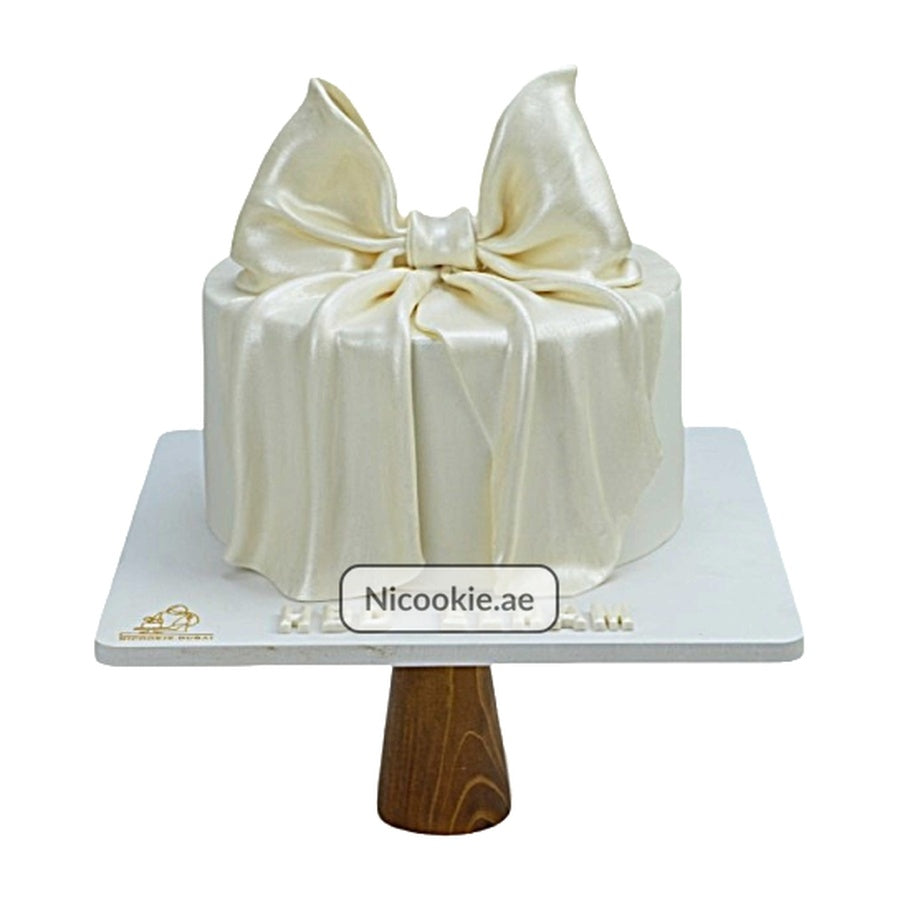 Ivory satin bow cake on a wooden cake stand.