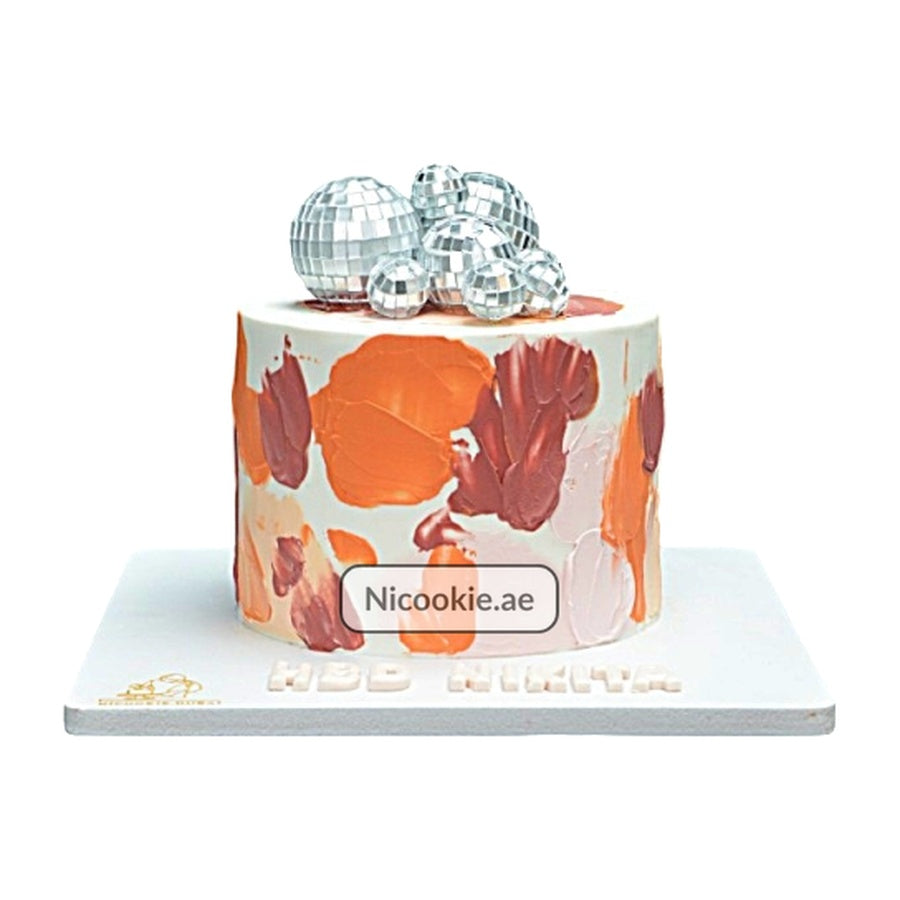 A round cake with abstract coral, terracotta, and peach frosting, topped with disco balls.