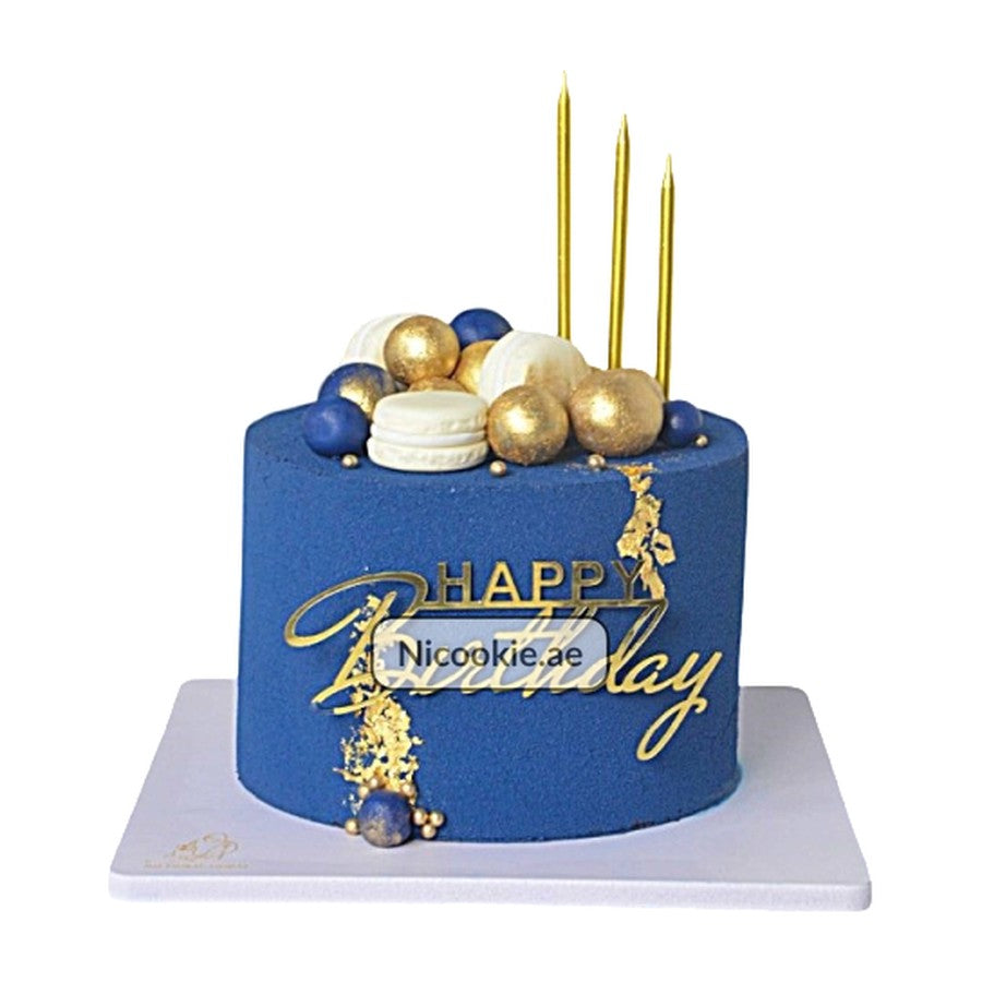Navy blue birthday cake with gold accents, macarons, spheres, and candles.