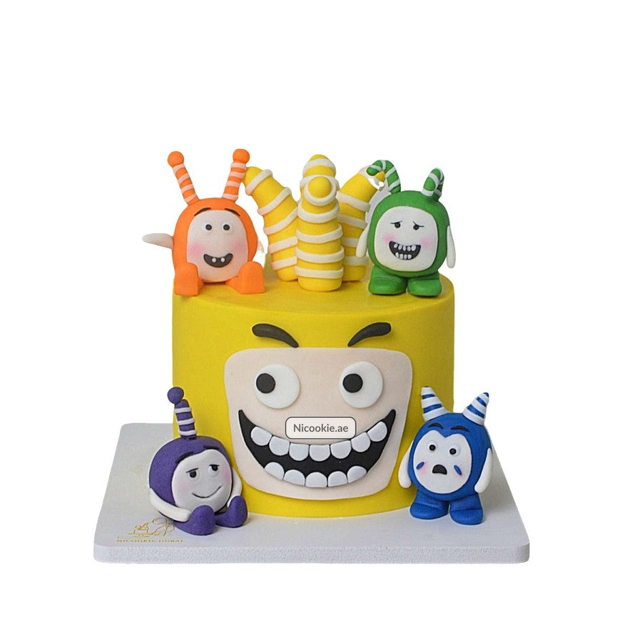 A yellow cake decorated with Oddbots characters and a large cartoon face.