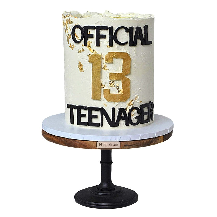 A white cake with "OFFICIAL 13 TEENAGER" in black and gold lettering.