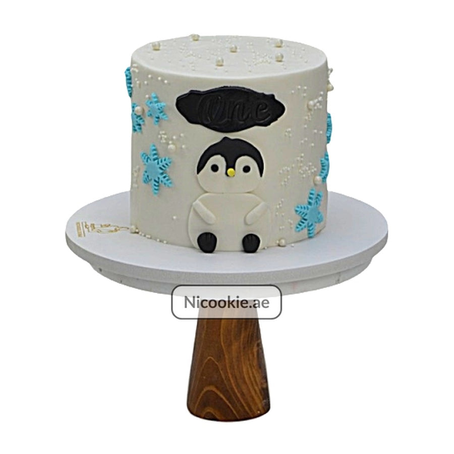 A white cake with a penguin and snowflakes for a first birthday.