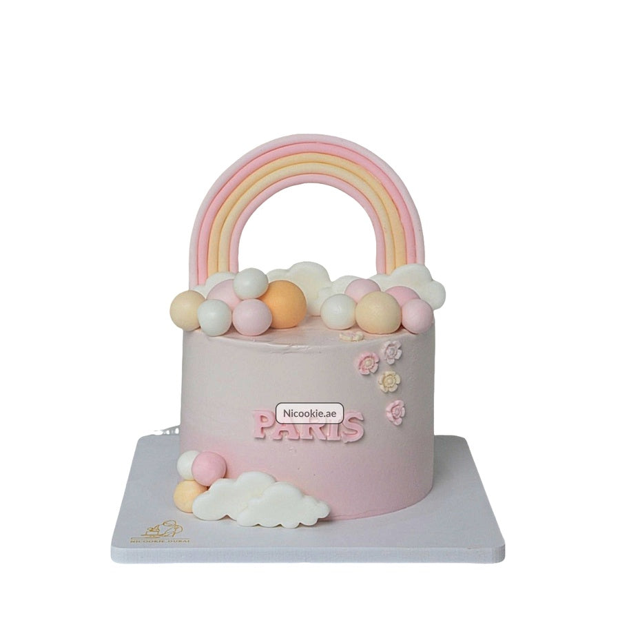 A pink cake with a rainbow, clouds, and pastel spheres.