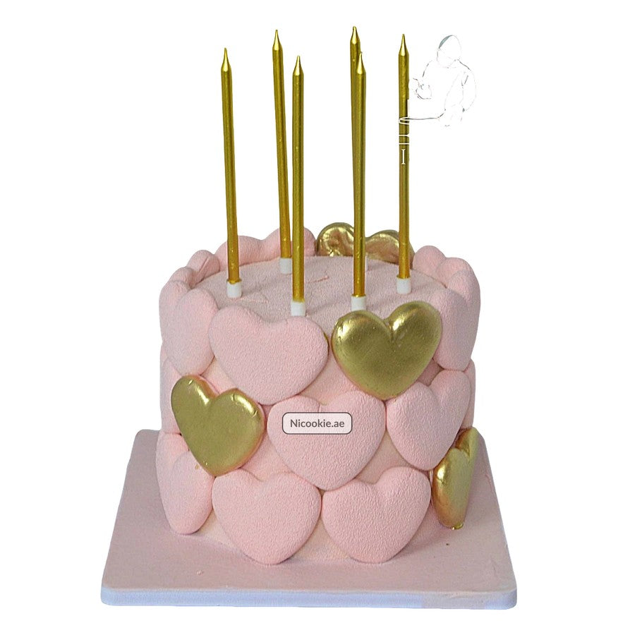 Pink cake decorated with pink and gold hearts and gold candles.