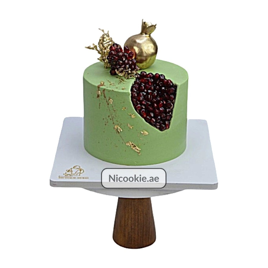 A green cake decorated with a realistic pomegranate slice, gold pomegranate, and gold foil.
