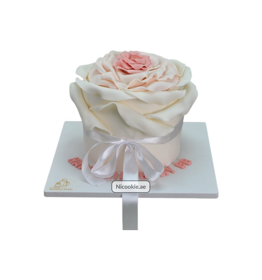 A white cake decorated with pink and white rose petals and a satin ribbon.