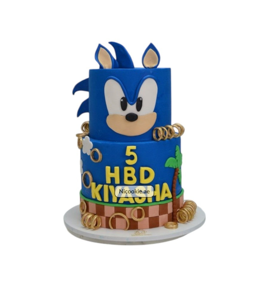 A two-tiered Sonic the Hedgehog birthday cake with gold rings and a checkered base.