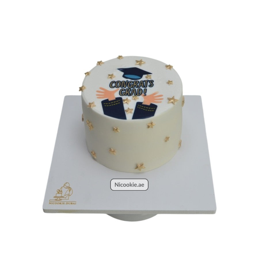 A white cake decorated with golden stars and a graduation cap design.