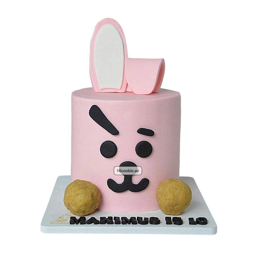 A pink bunny cake with black fondant features and two round treats.