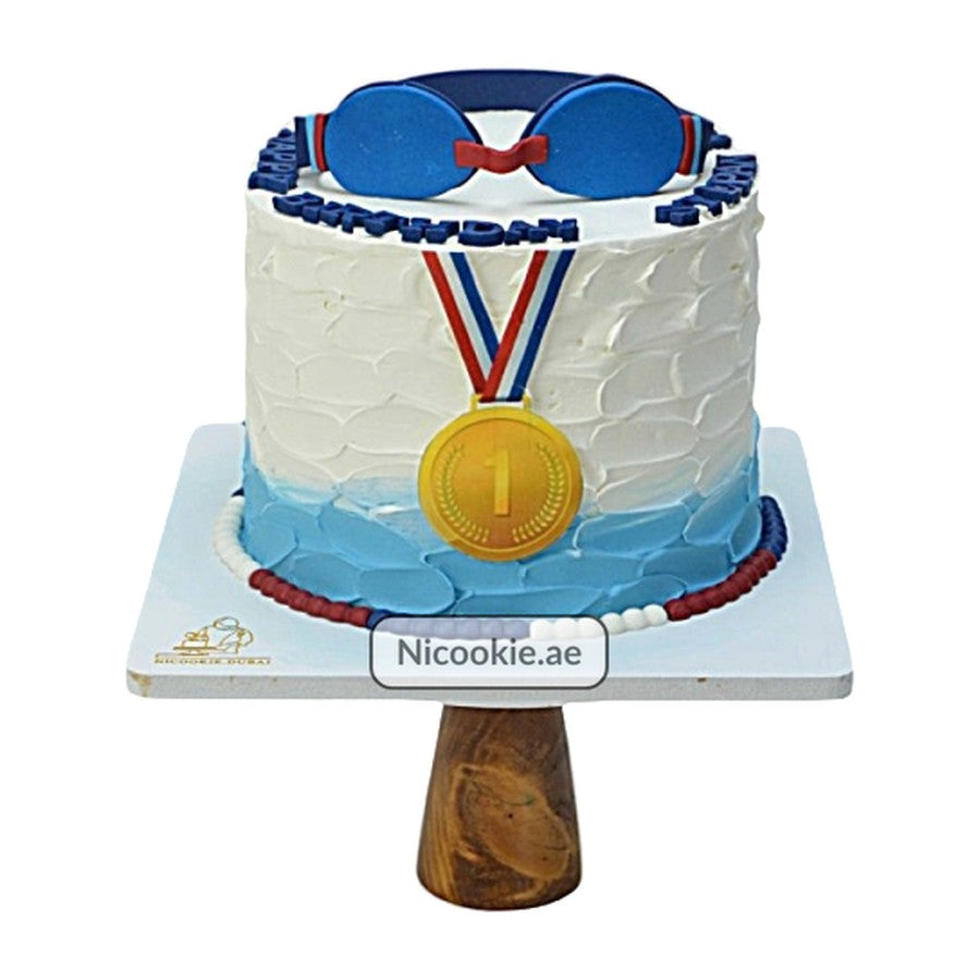 A swimming medal themed cake with blue goggles and a gold medal.