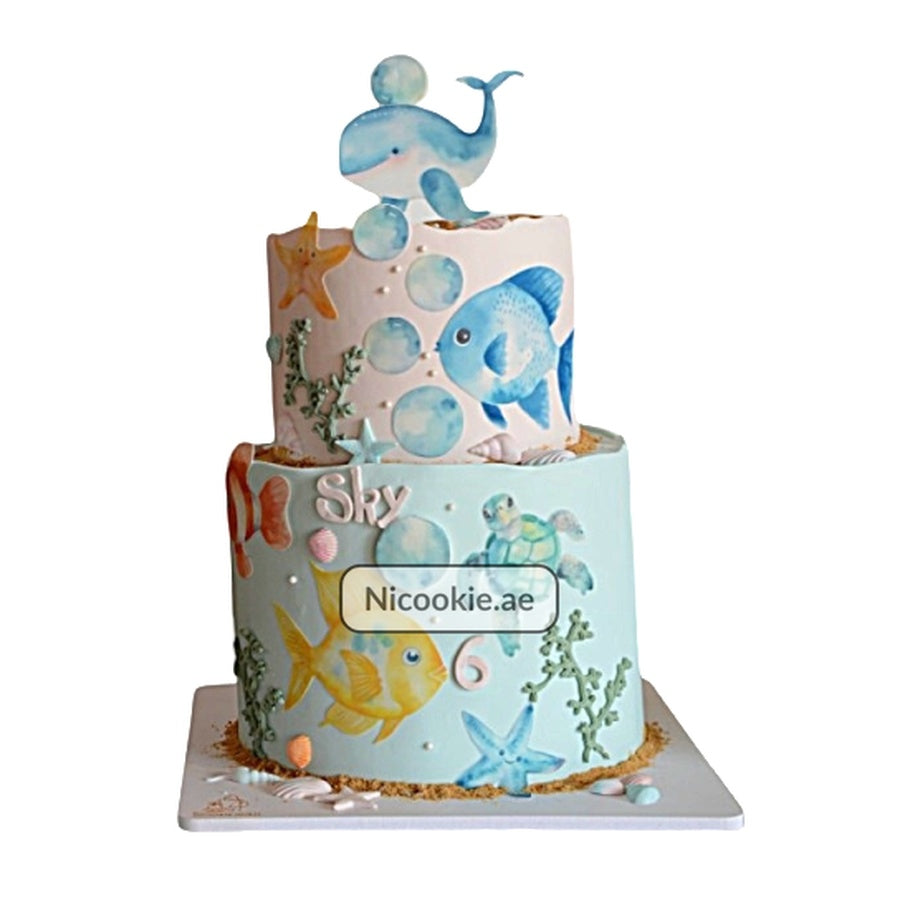 Two-tier underwater sea life cake with whale topper and ocean creatures.