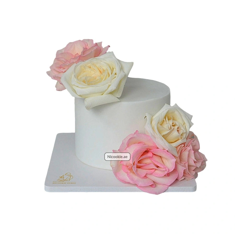 A white cake decorated with pink and ivory roses.
