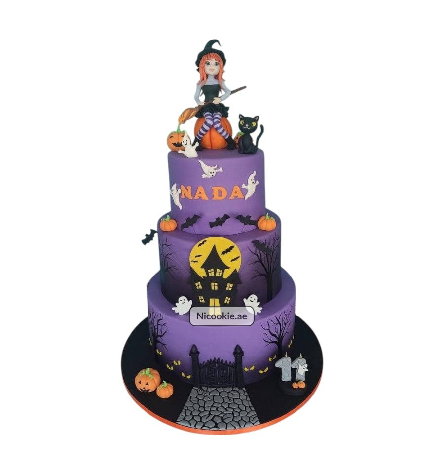 A three-tiered Halloween cake with a witch, black cat, ghosts, pumpkins, and a haunted house.